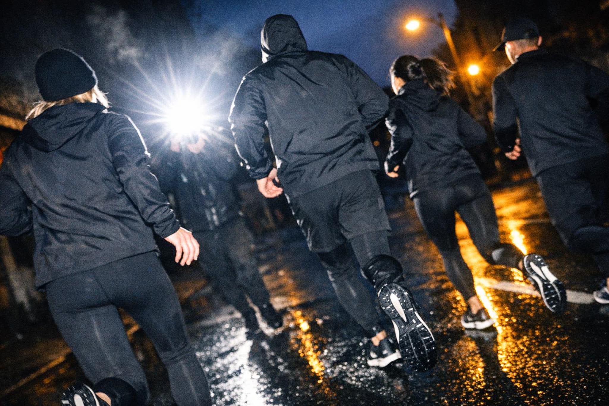 A running crew crosses an empty city street at dawn, the skyline still dark behind them
